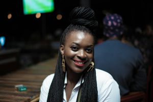 Black woman with braided hair and bright smile sitting indoors.